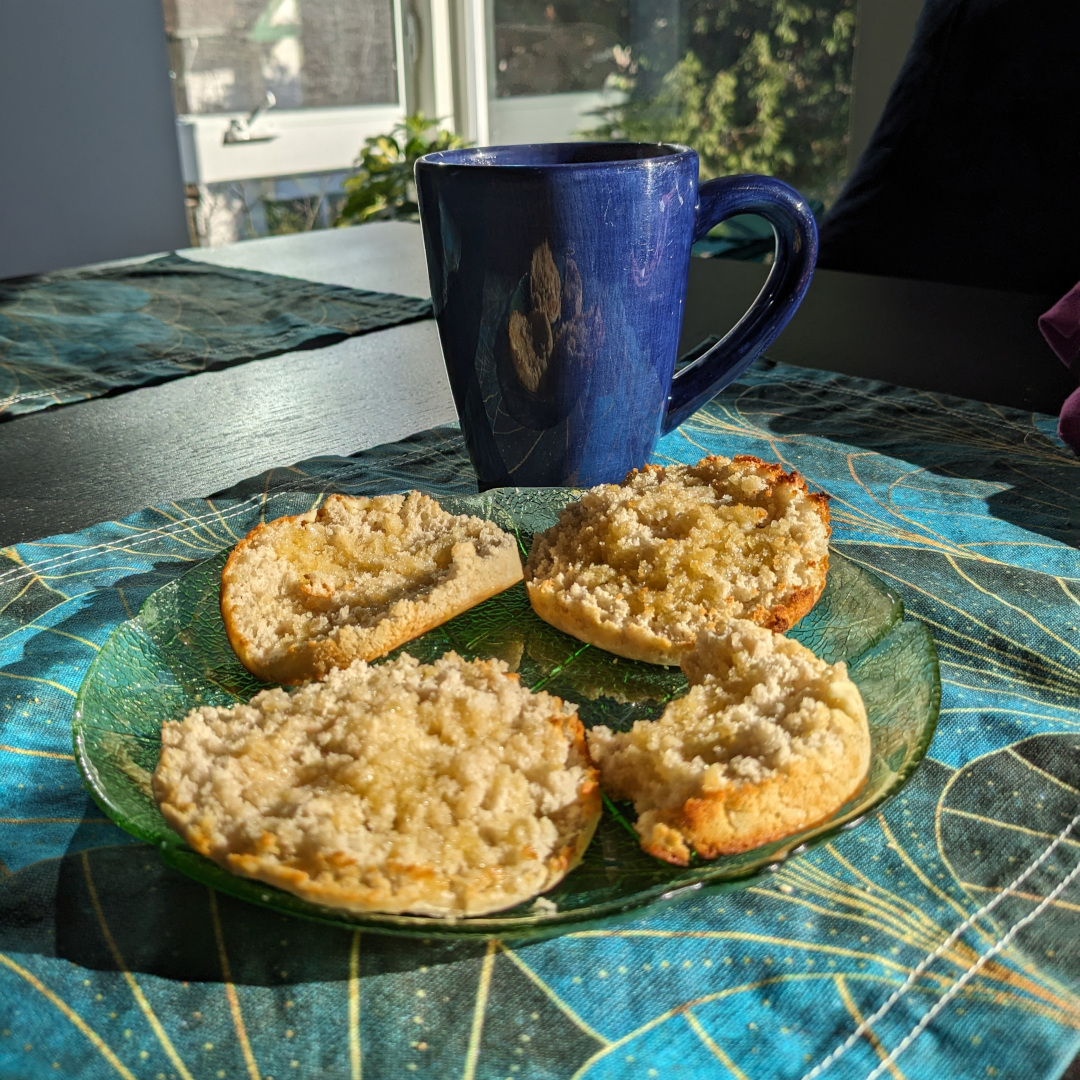 Split crumpets on a plate in the sun next to a cup of tea